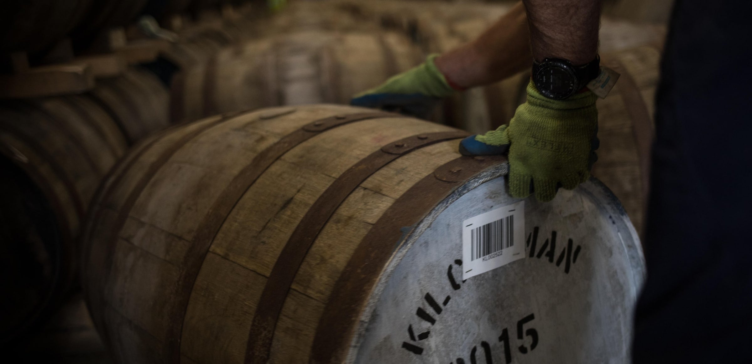 Person wearing gloves moving a barrel of whisky with a bar code covering some letters