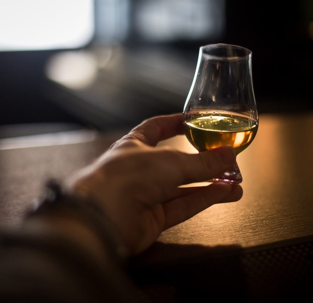 Whisky glass containing some whisky in the hand of someone resting on a table